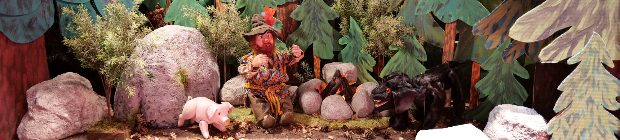 Der gutmütige Räuber Rotschopf sitzt mit Hund und Schwein am Feuer vor einem dunklen, dichten Wald.