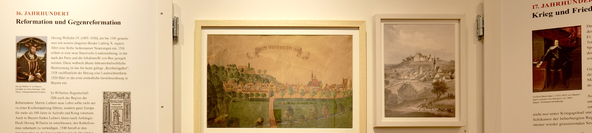 Die Tafel links stellt das 16. Jh. mit Reform und Gegenreformation dar. In der linken Bildmitte an der Wand hängt eine Abbildung des Marktes Mainburg.