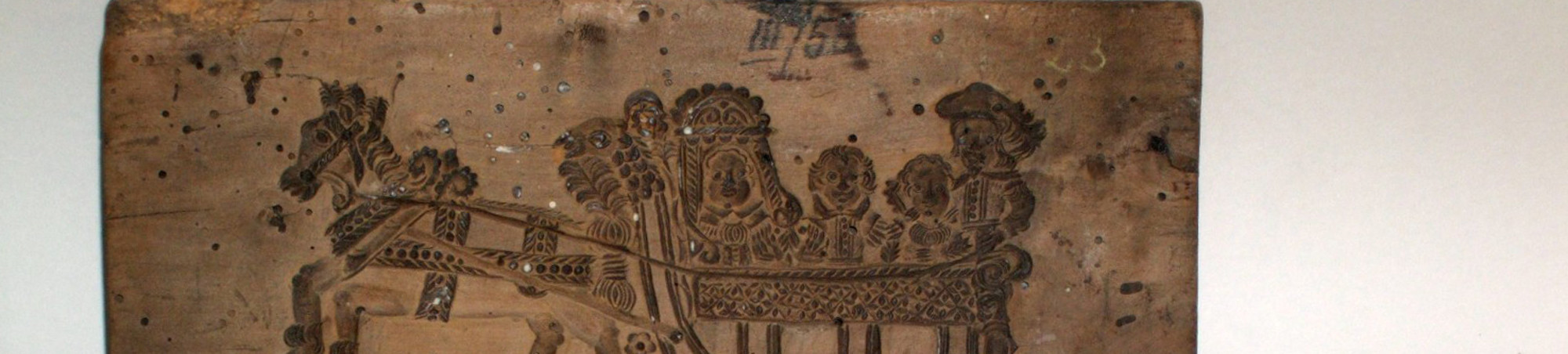 Querrechteckiger Holzstock, der auf beiden Seiten mit einer negativ geschnittenen Darstellung versehen ist. Auf der Vorderseite ist ein Schlitten dargestellt, auf dem drei Personen sitzen, einer steht. Vor den Schlitten ist ein reich geschmücktes Pferd gespannt. In den stilisiert dargestellten Schnee befindet sich die Signatur und Jahreszahl &quot;16 BP 44&quot;. Auf der Rückseite ist eine Kutsche dargestellt, in der ein Mann und eine Frau sitzen. Vor die Kutsche ist ein Pferd gespannt, auf dem ein Reiter sitzt. Zu seinen Füßen ursprünglich ein Hund.