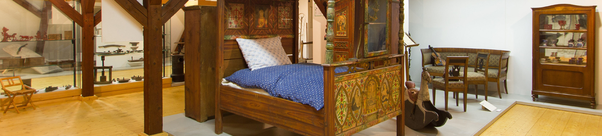 reich verziertes und bemaltes Himmelbett im Vordergrund, Schaukelpferd, Esszimmereinrichtung