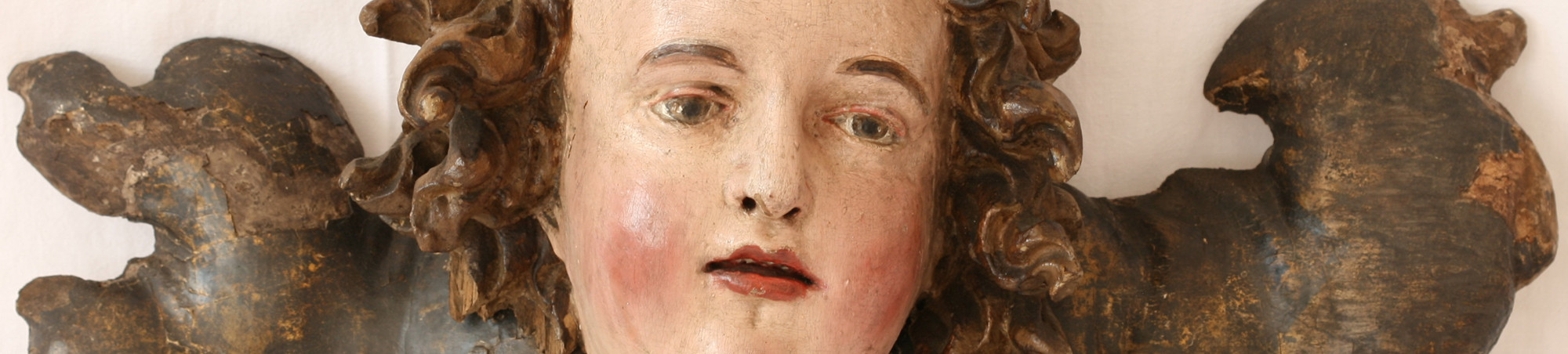 Lackierter Engelskopf mit stark bewegten Locken, auf stilisiertem Flügel aufgenagelt. Flügel braun gefaßt. Renaissance Stil.