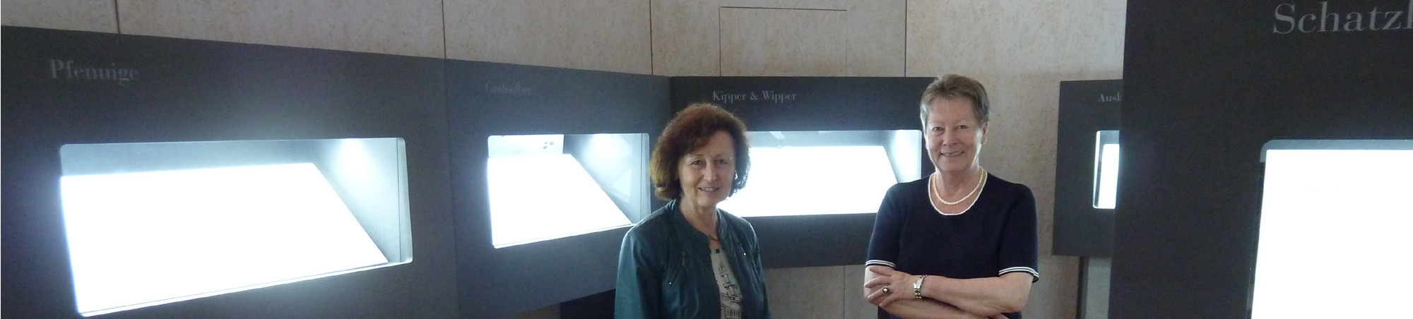 Zwei Frauen vor den beleuchteten, schwarzen Vitrinen.