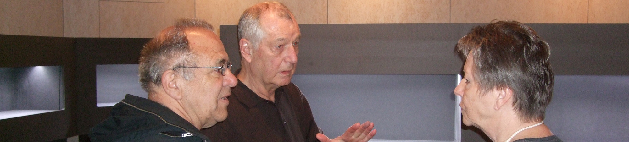 Drei Personen stehen vor beleuchteten, schwarzen Vitrinen und diskutieren.