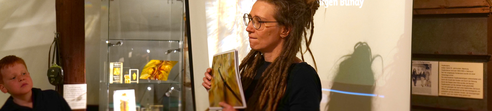 Die Biologin h&auml;lt Din-A4 Karten hoch mit Motiven aus dem Film und l&auml;sst sie sich von den Kindern erkl&auml;ren.