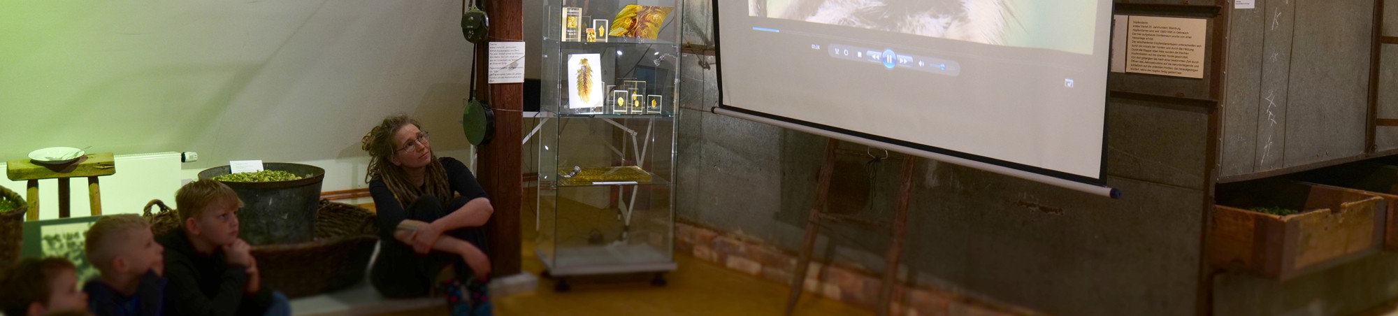 Die Kinder und die Biologin sitzen in der verdunkelten Hofenausstellung und sehen den Film an.