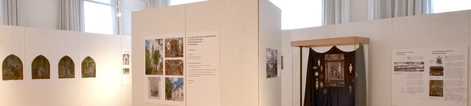 Die Raummitte wird von eine großen, dreieckigen Säule gebildet, um einen Rundgang zu schaffen. Links davon befinden sich vier bemalte Metalltafeln mit dem Leidensweg Christi. Rechts steht eine Glasvitrine mit Exponaten aus der Glaubenswelt vor hellen Ausstellungwänden. Violette Akzente und sparsam eingesetzte, farbige Abbildungen vermitteln einen feierlich-heiteren Eindruck.