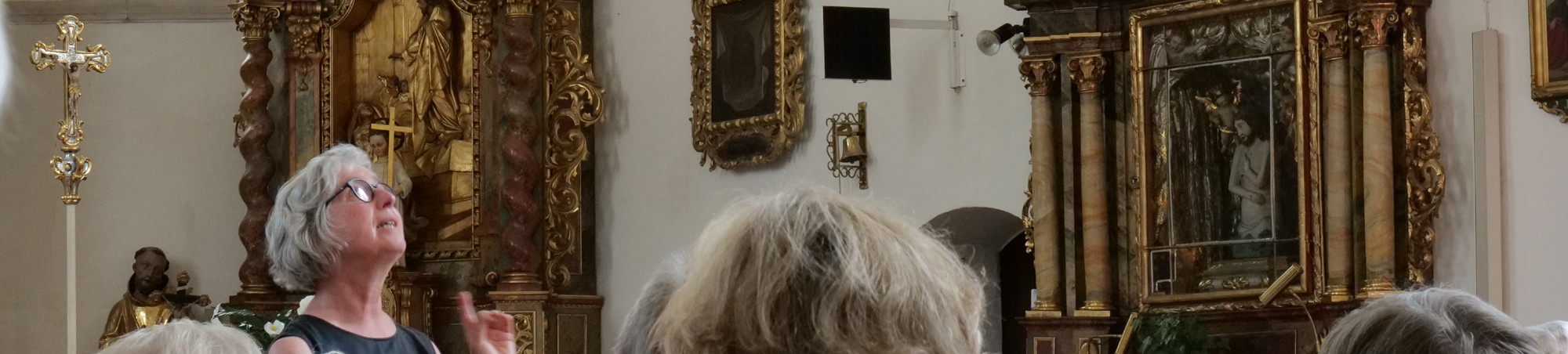 Eine Frau blickt zur Kirchendecke und weist mit dem Zeigefinger auf das, was sie erkl&auml;rt.