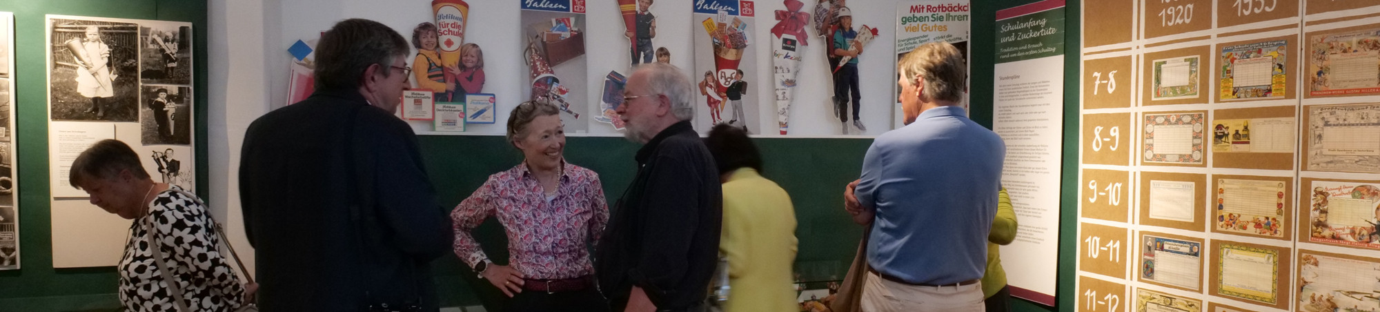 3. von rechts unterh&auml;lt sich mit Besucher. Drei weitere Personen besichtigen die Ausstellung.