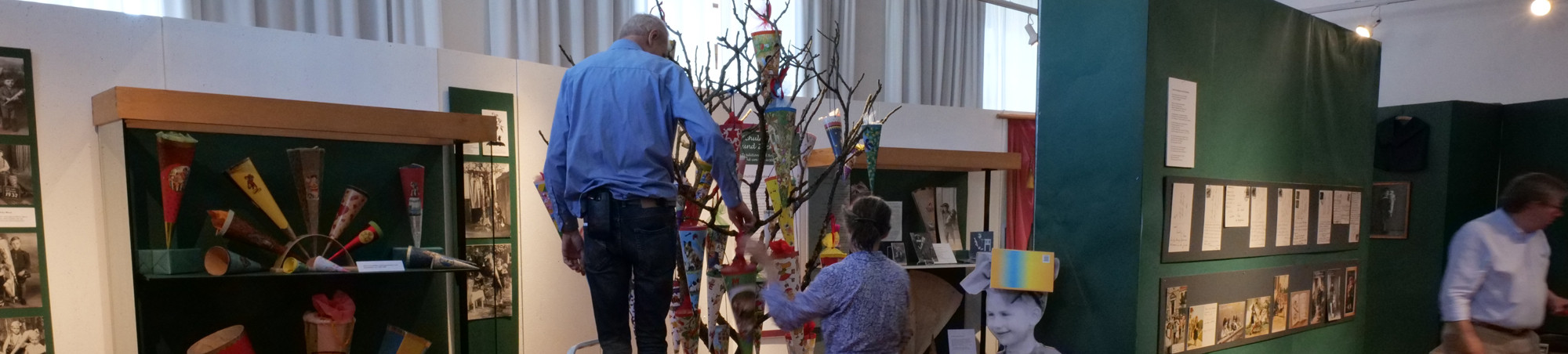 Zwei Personen h&auml;ngen Zuckert&uuml;ten auf. Eine Person verl&auml;sst den Bildraum.