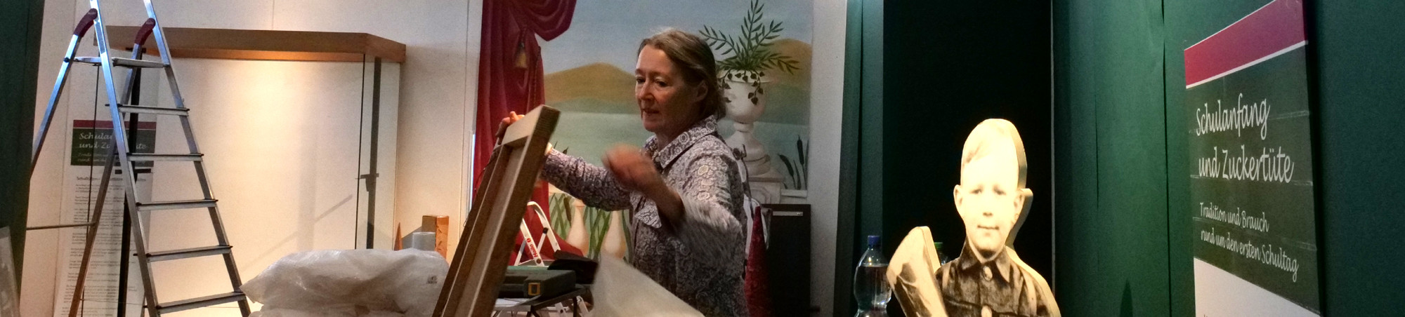 Eine Leiter, eine leere Vitrine, im Mittelpunkt eine Frau, die ein Exponat auspackt.