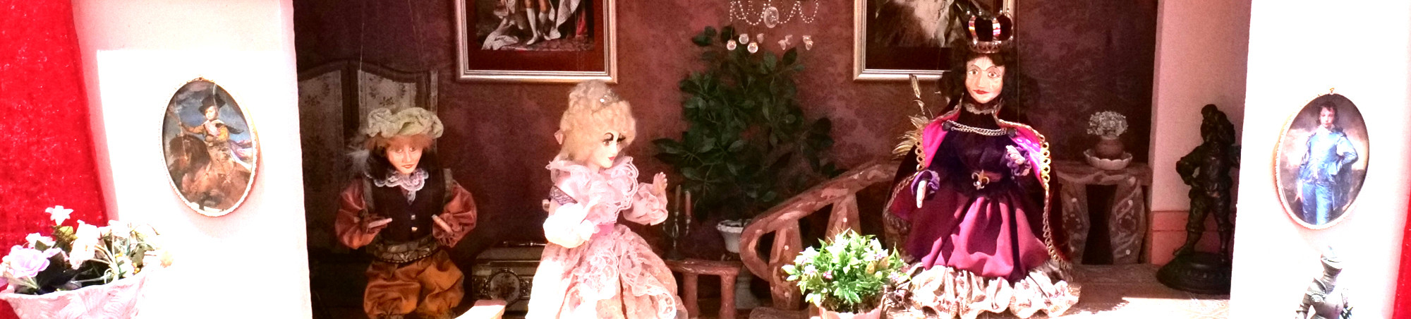 In einem barocken Schloss mit Kronleuchter und Ahnenbildern sitzt der König auf einem Podest und mit einigen Abstand neben ihm stehen Prinzessin und Diener.